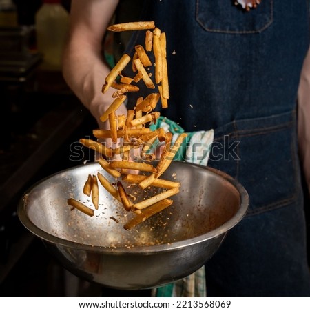 A person tossing freshly cooked fries with spices on a mixing bowl