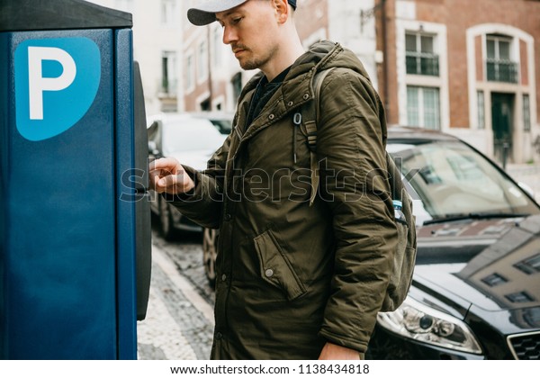 A person or a tourist pays for car parking in a\
street parking machine