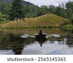 Person in traditional Norwegian clothing  rowing a wooden boat on a calm pond surrounded by lush greenery, rolling hills, and forest in Norway, reflecting the tranquil rural landscape on a cloudy day