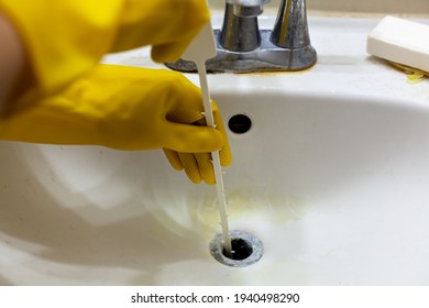 A Person Is Trying To Unclog The Drain Of A Sink Using Plastic Disposable Snake Auger Tool Which Helps Pull Hair And Soap Debris From The Sinkhole. Close Up DIY Home Maintenance Concept. 