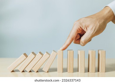 A person use finger stopping wood pieces of a domino effect. Concept of risk management, risk protection, crisis  and investment protection