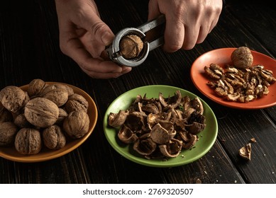 A person uses a nutcracker to open walnuts at a kitchen table. Some uncracked walnuts are on one plate while pieces of nuts are on another.