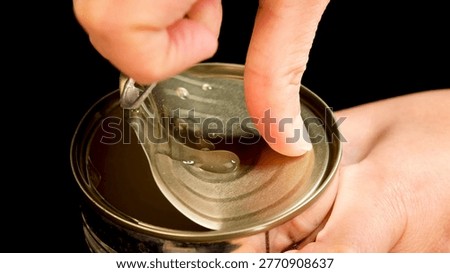 A person uses a pull tab to open a tin can against a black background.