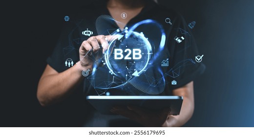 A person uses a tablet displaying glowing B2B icons and digital interface elements on a dark background. Concept of business, technology, and collaboration