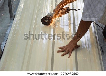 A person is using an angle grinder to cut a metal sheet in a workshop. Sparks are flying as the tool makes contact with the metal.