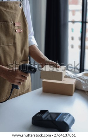 A person using a barcode scanner to scan a small cardboard box in a retail shop for inventory management or preparing an order for shipping.