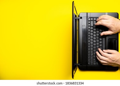 Person Using Black Laptop On A Yellow Desk. Above View. Copy Space. Studio Shot. Corporate Workplace Concept.