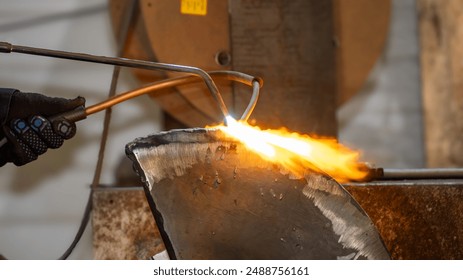 A person is using a blowtorch to heat a piece of metal. Concept of craftsmanship and skill, as the person carefully works with the hot metal - Powered by Shutterstock