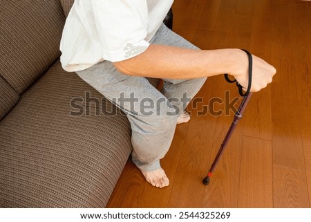 A person using a cane to stand up from a sofa