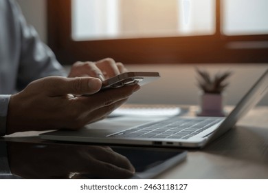 A person is using a cell phone while sitting at a desk with a laptop and a potted plant. Concept of productivity and focus, as the person is engaged in work or communication on their devices