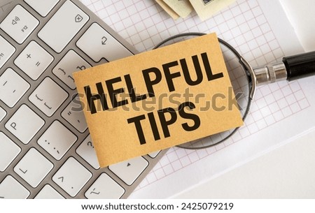 A person is using a computer keyboard and a magnifying glass. The keyboards keys are labeled with useful tips for better use. The magnifying glass helps in reading them clearly.