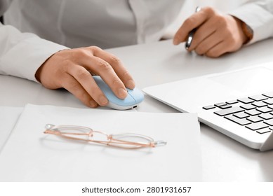 Person using computer mouse next to laptop and glasses