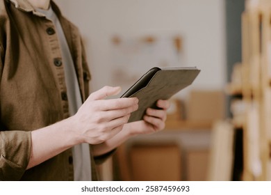Person using digital tablet while standing in modern office setting, focusing on work-related tasks with shelves in background
