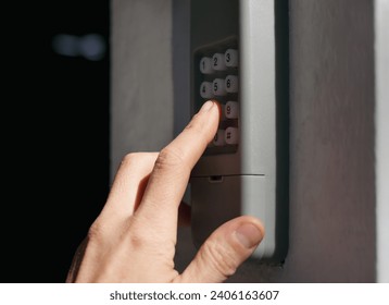 Person using garage door keypad or keyless door access number pad. Gray waterproof box mounted on outside wall of home or building. Used for coded access to open doors or gates. Selective focus.
