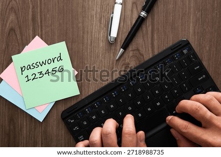 Person using a keyboard while a sticky note with a weak password sits on a wooden desk