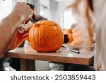 Person using a knife to carve a face design into a pumpkin in preparation for Halloween, pumpkin carving workshop