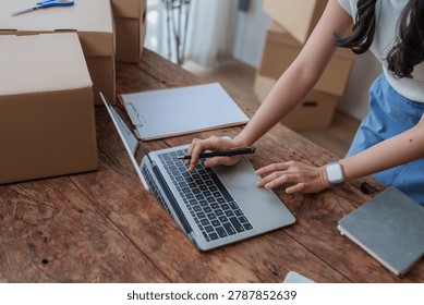 Person using laptop computer for e commerce with shipping boxes on wooden desk