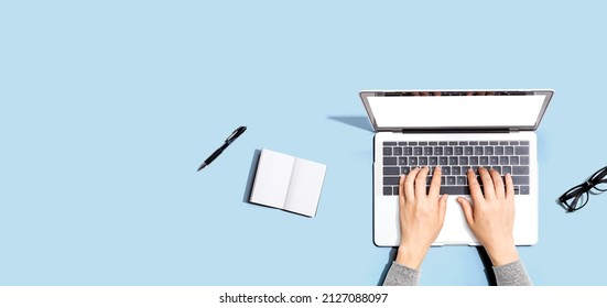 Person using a laptop computer with a notebook and eyeglasses - Flat lay