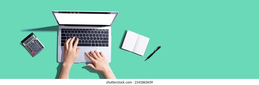 Person Using A Laptop Computer With A Notebook And A Calculator