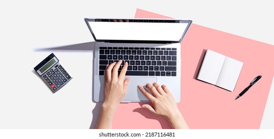 Person Using A Laptop Computer With A Notebook And A Calculator - Flat Lay