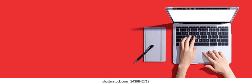 Person using a laptop computer with a notebook - Flat lay