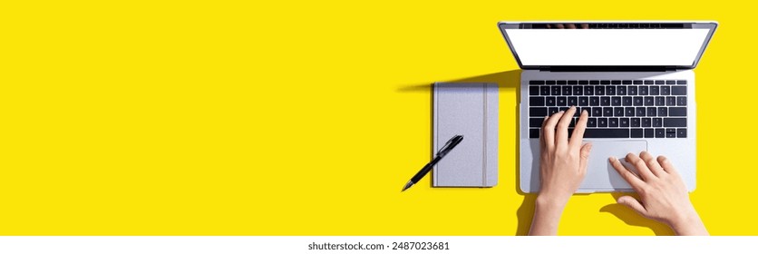 Person using a laptop computer with a notebook - Flat lay