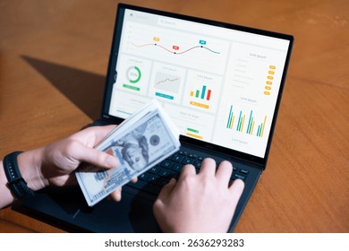 A person is using a laptop to input money into a graph. The graph shows the value of the money over time