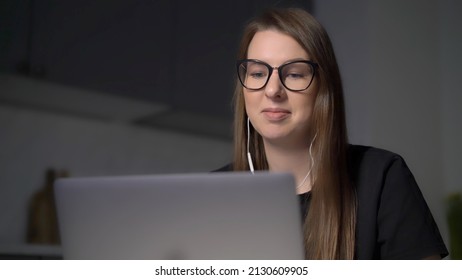 Person Using Laptop. Woman Working On The Computer In Kitchen. Remote Work Or Study From Home. Girl In Glasses At Night. Video Conference Call Meeting. Female Chat In Headphones Use Web Camera.