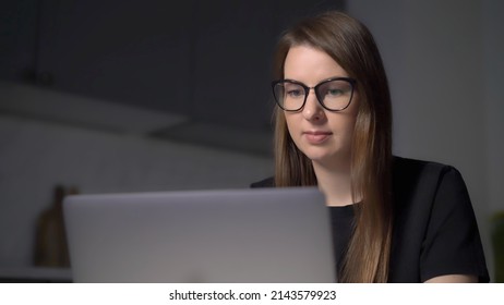 Person Using Laptop. Woman Working On The Computer, Typing Text On Keyboard. Electronic Device, Tablet On Table In The Kitchen. Remote Work Or Study From Home. Girl In Glasses At Night.