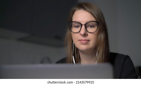 Person Using Laptop. Woman Working On The Computer In Kitchen. Remote Work Or Study From Home. Girl In Glasses At Night. Video Conference Call Meeting. Female Chat In Headphones Use Web Camera.