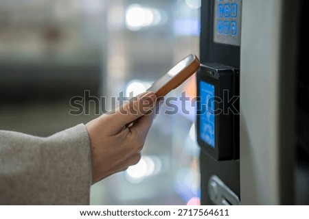 Person using mobile device for digital transaction, tapping near a payment terminal or vending machine, illustrating modern, convenient shopping and secure financial technology