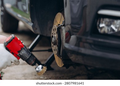 Person using power drill with wire brush attachment cleaning corroded brake disc of a car during maintenance and repair work