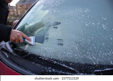 Person using a scrapper to scrape off icy and frost from the window of a red car.
