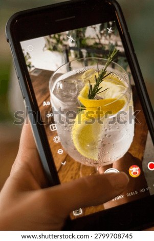 A person using a smartphone to take a top-down picture of a fresh gin cocktail glass on a restaurant table.