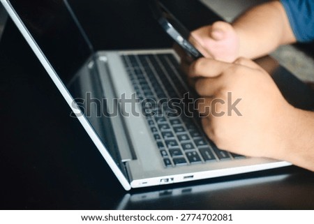 A person using a smartphone while sitting in front of an open laptop, highlighting multi-device usage and digital connectivity.