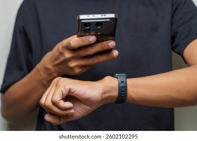 Person using a smartphone while wearing a smart watch on their wrist against a neutral background