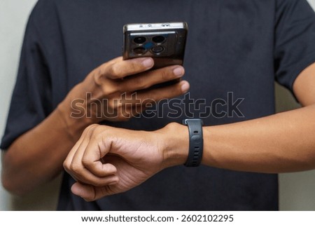 Person using a smartphone while wearing a smart watch on their wrist against a neutral background