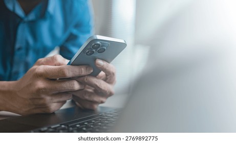 Person using smartphone while working on laptop, representing mobile communication, social media interaction, and digital lifestyle with online messaging, fintech apps, and modern technology usage.