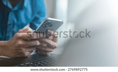 Person using smartphone while working on laptop, representing mobile communication, social media interaction, and digital lifestyle with online messaging, fintech apps, and modern technology usage.