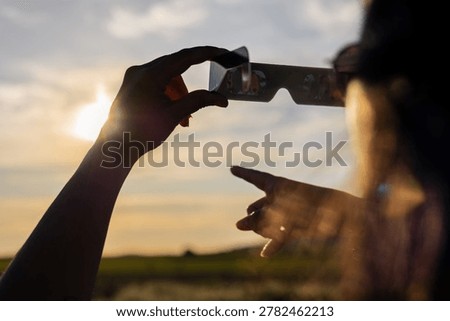 Person using solar eclipse glasses to safely observe the sun during a celestial event, preventing eye damage outdoors