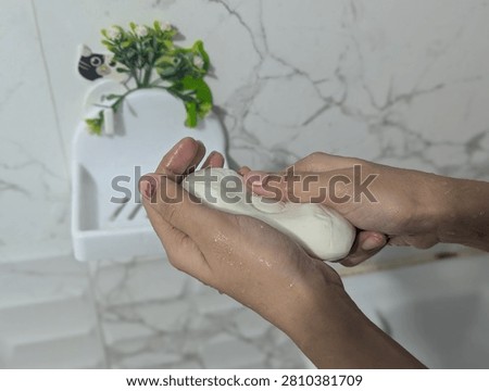 Person using a solid soap bar for hand hygiene in front of a wall background.