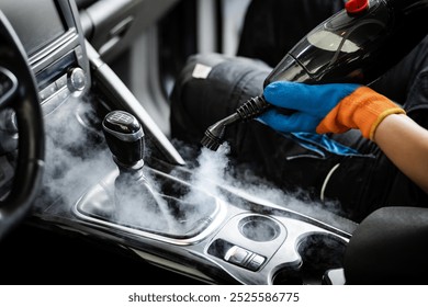 A person is using a steam cleaner inside a car, focusing on the gear shift area, releasing steam to eliminate stains and disinfect surfaces effectively.