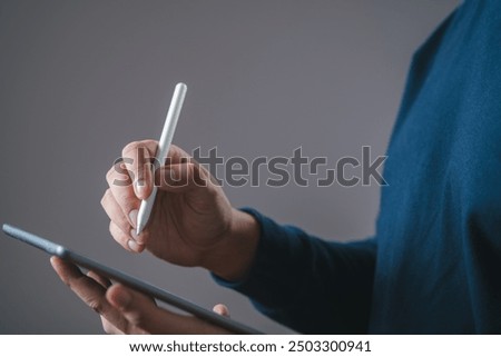 A person using a stylus to write or draw on a digital tablet, highlighting modern technology in everyday tasks.