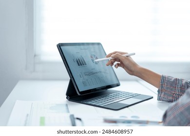 A person is using a tablet to draw a graph. The graph is showing a downward trend