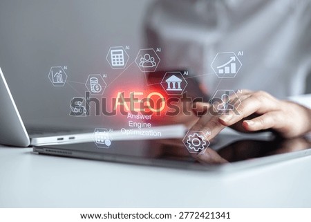 A person is using a tablet while sitting at a desk with a laptop. Various icons representing answer engine optimization appear on the tablet screen. It is daytime.