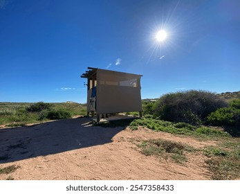 Person using tin outhouse in rural Quobba Station, Western Australia. Outdoor toilet, rustic country setting, dirt, grass, clear blue sky, rural Australia, rustic lifestyle. - Powered by Shutterstock