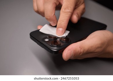 A person is using a tissue to clean a cell phone, emphasizing hand gesture, finger action, communication device care, and gadget maintenance