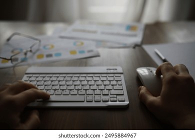 Person Using Wireless Keyboard and Mouse in Modern Office Setting with Documents on Desk