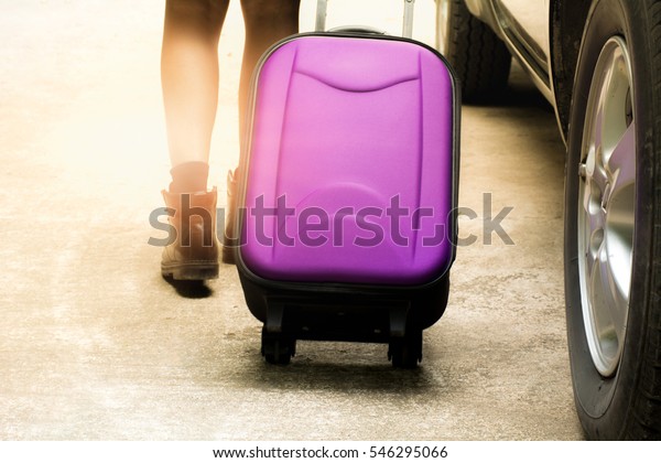 Person walk drag purple travel bag beside black car\
for travel and sun light