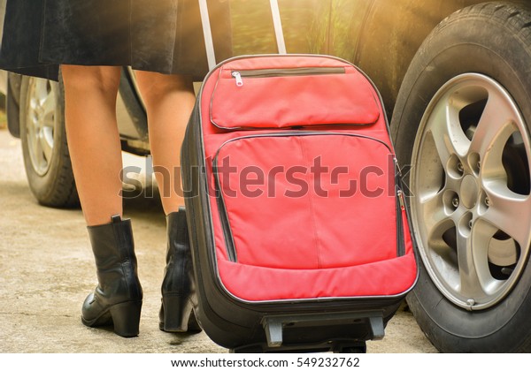 Person walk drag red travel bag beside black car\
for travel and sun light